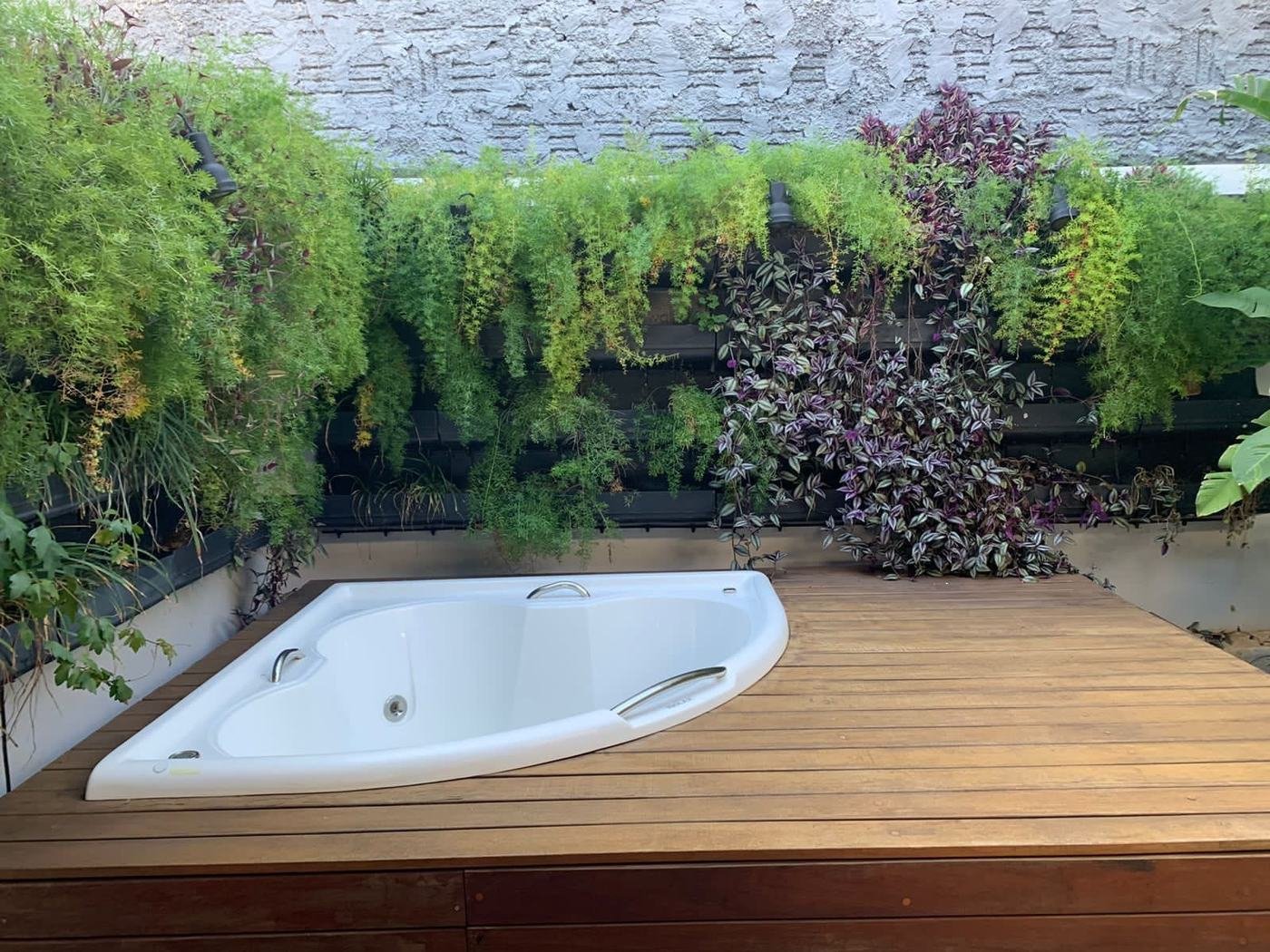Banheira de canto instalada em deck de madeira com jardim vertical